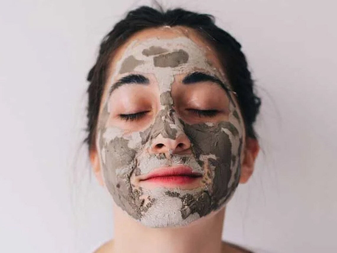 Person with a mud mask on their face against a plain background