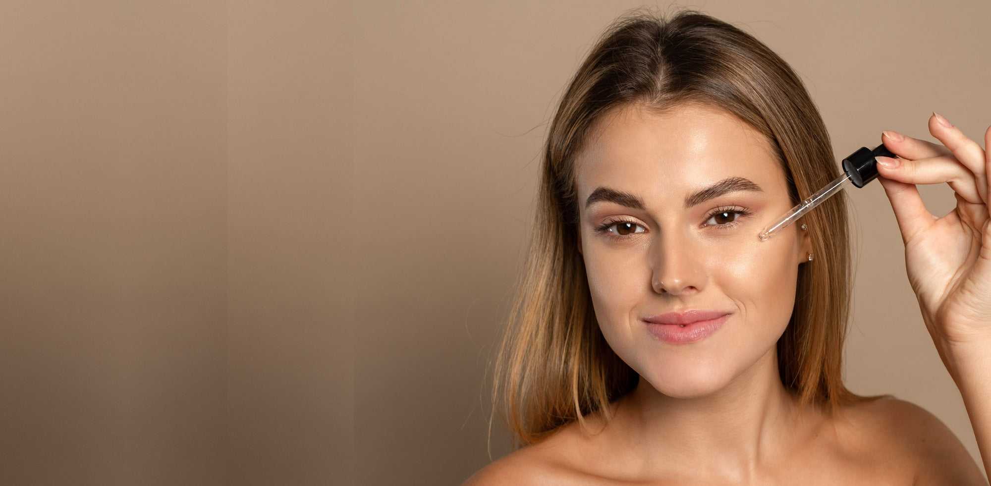 Woman applying skincare product with a dropper on a beige background