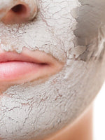 Close-up of a person applying a clay facial mask to their face.